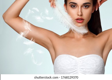 Armpit epilation, hair removal. Young woman holding her arms up and showing clean underarms, depilation smooth clear skin . Beauty portrait. armpit's care. Large white feather near skin