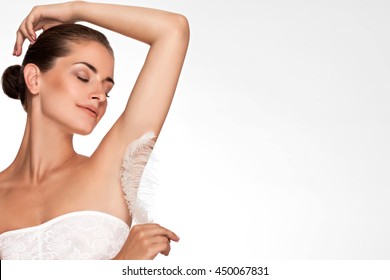 Armpit epilation, hair removal. Young woman holding her arms up and showing clean underarms, depilation smooth clear skin . Beauty portrait. armpit's care. Large white feather near skin