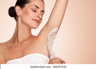 Armpit epilation, hair removal. Young woman holding her arms up and showing clean underarms, depilation smooth clear skin . Beauty portrait. armpit's care. Large white feather near skin