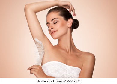 Armpit epilation, hair removal. Young woman holding her arms up and showing clean underarms, depilation smooth clear skin . Beauty portrait. armpit's care. Large white feather near skin