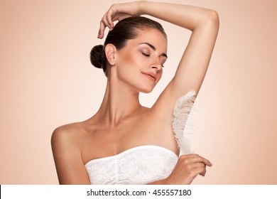 Armpit Epilation, Hair Removal. Young Woman Holding Her Arms Up And Showing Clean Underarms, Depilation Smooth Clear Skin . Beauty Portrait. Armpit's Care. Large White Feather Near Skin