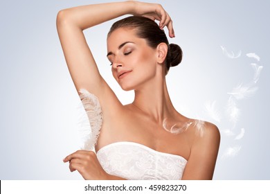 Armpit epilation, hair removal. Young woman holding her arms up and showing clean underarms, depilation smooth clear skin . Beauty portrait. armpit's care. Large white feather near skin