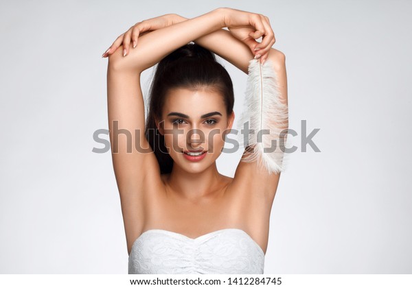Armpit epilation, hair removal. Young woman holding\
her arms up and showing clean underarms, depilation smooth clear\
skin . Beauty portrait. armpit\'s care. Large white feather near\
skin