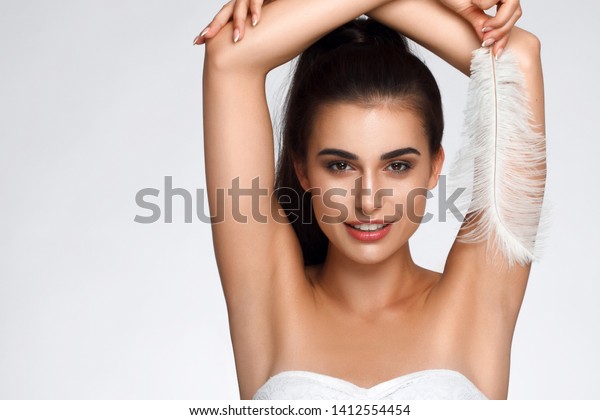 Armpit epilation, hair removal. Young woman holding
her arms up and showing clean underarms, depilation smooth clear
skin . Beauty portrait. armpit's care. Large white feather near
skin