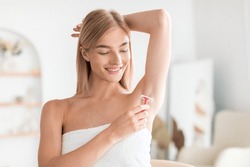 Armpit Hair Removal. Young Blonde Lady Shaving Armpits Using Safety Razor, Removing Hair In Bathroom At Home. Woman Making Underarms Depilation Raising Arm Standing Wrapped In Towel