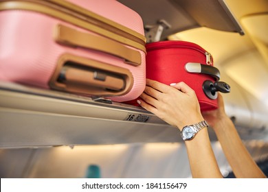 Arms shoving a small piece of luggage to the top shelf of an aircraft