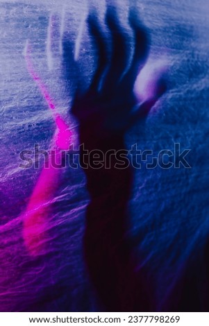  Arms of woman pressing against curtain. silhouette woman behind blue light poses mysteriously and artistically