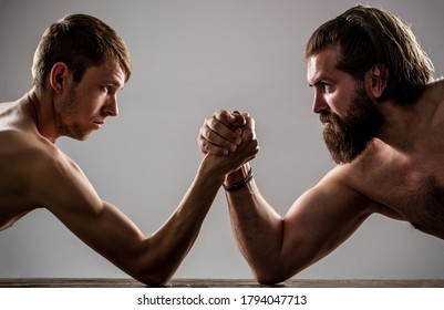 Arms Wrestling Thin Hand, Big Strong Arm In Studio. Two Man's Hands Clasped Arm Wrestling, Strong And Weak, Unequal Match. Heavily Muscled Bearded Man Arm Wrestling A Puny Weak Man.