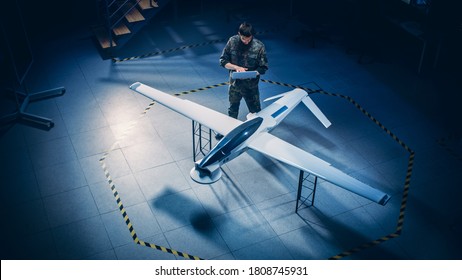 Army Aerospace Engineer Work On Unmanned Aerial Vehicle / Drone. Uniformed Aviation Expert Using Laptop. Industrial Facility With Surveillance, Warfare Tactics, Attack Machine. Elevated Shot