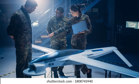 Army Aerospace Engineers Work On Unmanned Aerial Vehicle / Drone. Uniformed Aviation Experts Talk, Using Laptop. Industrial Facility With Aircraft For: Surveillance, Warfare Tactics, Air Strike