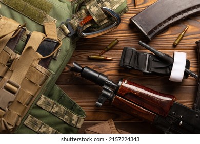 Army Body Armor, Helmet And Ammunition, Kalashnikov Assault Rifle With Matrons And First Aid Tourniquet Composition On Brown Wood. Army Body Armor. Flat Laying. Military Concept.