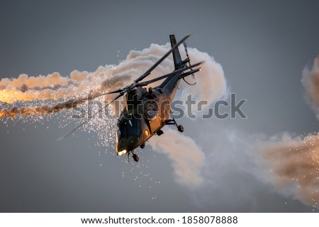 Army helicopter in flight firing off defensive flare decoys at dusk.