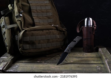 Army Knife With Black Blade And Olive Handle. Green Knife For The Military And A Green Backpack With A Molle System. Thermos In A Leather Case.