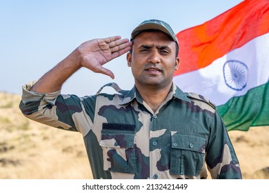 army officer saluting by looking at camera in front of waving Indian flag - conept of patriotism, respect and pride.