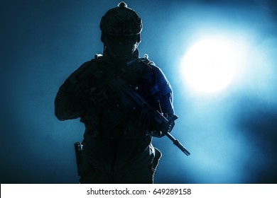 Army Soldier In Protective Combat Uniform Holding Special Operations Forces Combat Assault Rifle. Studio Shot, Backlit Silhouette