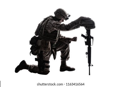 Army soldier in sorrow for fallen comrade, standing on knee, leaning on rifle with helmet and two dog tags on chain, studio shoot isolated on white low key silhouette. Military funeral honors, grief
