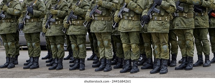 Army soldiers in uniform stand in formation on a concrete surface with yellow crosswalk lines. They wear combat fatigues and boots, showing discipline and readiness. - Powered by Shutterstock