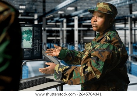 Army tech specialist in data center and coworker at workstation troubleshooting military computer systems. Soldier and command center server room admin looking at intel on display