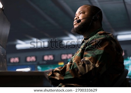 Army telecommunication systems agent using radio and satellite equipment, providing combat support using headset mic. Soldier managing communications networks, talking in microphone