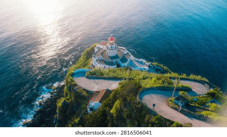 Arnel lighthouse standing on a dramatic cliff with ocean and winding road at dusk