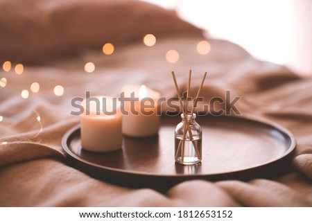 Aroma bamboo sticks in bottle with scented liquid with candles staying on wooden tray in bed closeup. 