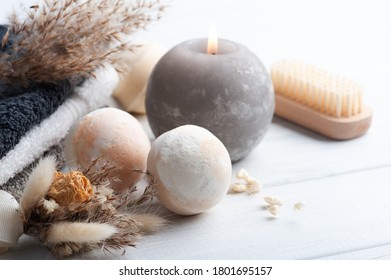 Aroma bath bombs in spa composition with dry flowers and towels. Aromatherapy arrangement, zen still life with grey lit candle and body brushes
