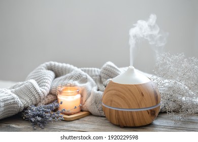 Aroma composition with a modern aroma oil diffuser on a wooden surface with a knitted element, candle and lavender.