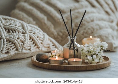 Aroma diffuser, burning candle, cherry blooming flowers and perfume on wooden bamboo tray. Cozy home decor, hygge and aromatherapy concept. Comfortable atmosphere, spring delicious fresh smell