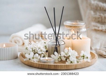 Aroma diffuser, burning candle, cherry blooming flowers and perfume on wooden bamboo tray. Cozy home decor, hygge and aromatherapy concept. Comfortable atmosphere, spring delicious fresh smell