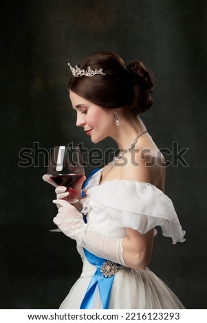 Aroma and flavor. Young elegant woman in image of princess or viscountess tasting red wine isolated on dark vintage background. Comparison of eras concept, fashion, art, ad.