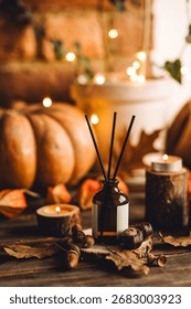 Aroma reed diffuser, pumpkins, knitted warm sweaters, candles, dry leaves on wooden table. Concept of house decor, apartment seasonal fragrance. Thanksgiving. Autumn mood, cozy fall home atmosphere