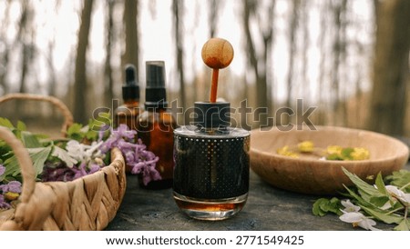 Aromatherapy diffuser and amber glass bottles with herbs and flowers arranged on a rustic wooden table outdoors