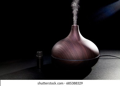 Aromatherapy. Essential Oil Aroma Diffuser Humidifier Diffusing Water Articles In The Air. Electric Ultrasonic Device Emitting Atomized Water Droplets Against Black Background With Copy Space.