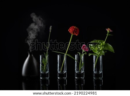Aromatherapy essential oils diffuser in front of flowers associated with the scent of the vapor coming out of the device