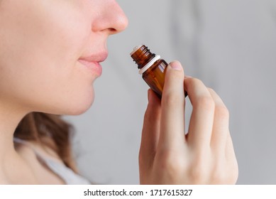 Aromatherapy: a girl with beautiful skin holds a bottle of essential oil near her nose and inhales. Close up, bright marble background.