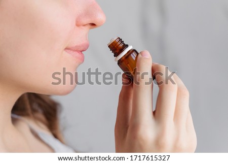 Aromatherapy: a girl with beautiful skin holds a bottle of essential oil near her nose and inhales. Close up, bright marble background.