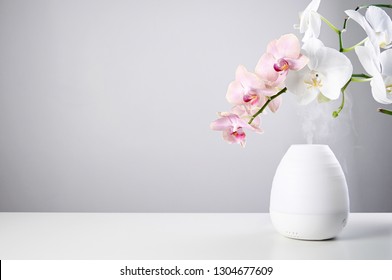 Aromatherapy at home. Ultrasonic Oil diffuser and orchid flowers on white table of gray background. Close up view with copy space