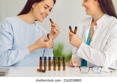 Aromatherapy. Joyful Young Woman Chooses Scent Of Essential Oil When Visiting Female Homeopathic Doctor. Woman Sniffs Scents Of Essential Oils Presented To Her By Friendly Female Doctor In Her Office.