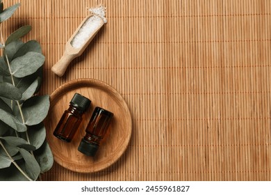 Aromatherapy products. Bottles of essential oil, sea salt and eucalyptus branches on bamboo mat, flat lay. Space for text - Powered by Shutterstock