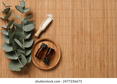 Aromatherapy products. Bottles of essential oil, sea salt and eucalyptus branches on bamboo mat, flat lay. Space for text - Powered by Shutterstock