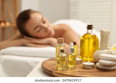 Aromatherapy. Woman relaxing on massage couch in spa salon, focus on bottles of essential oils, herbal bag, burning candle and stones - Powered by Shutterstock