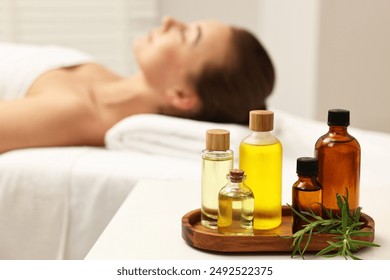 Aromatherapy. Woman relaxing on massage couch in spa salon, focus on bottles of essential oils and rosemary - Powered by Shutterstock