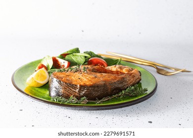 Aromatic baked salmon steak with juicy salad, tomatoes, lemon and fresh thyme on bright plate close up. Tasty and healthy food idea.