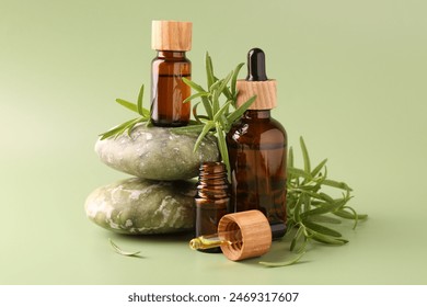 Aromatic essential oils in bottles, rosemary, pipette and pebble stones on green background