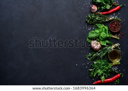 Aromatic fresh herbs and spices on a black slate, stone or concrete background. Top view with copy space.