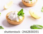 Aromatic homemade lemon tartlets with cream and mint leaves on white marble table close up.