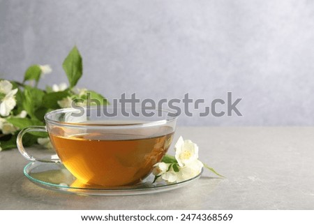 Aromatic jasmine tea in cup, flowers and green leaves on light grey table, space for text