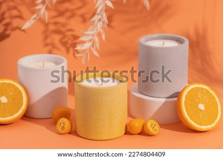 Aromatic premium soy candles in gray concrete jar on orange background with orange fruits and shadow. Poster banner for candle shop, beauty, spa