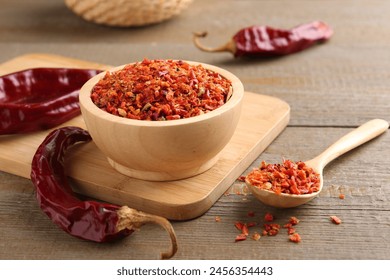 Aromatic spice. Red chili pepper flakes in bowl, spoon and pods on wooden table - Powered by Shutterstock