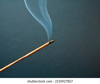 Aromatic stick isolated on black backdrop. Blue wavy smoke spreads in the air. Swirling movement of smoke. Single incense stick burning with red hot ash. Chinese Incense Stick